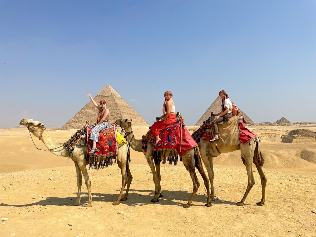 Three travellers riding camels in front of the Giza pyramids on a private Cairo tour
