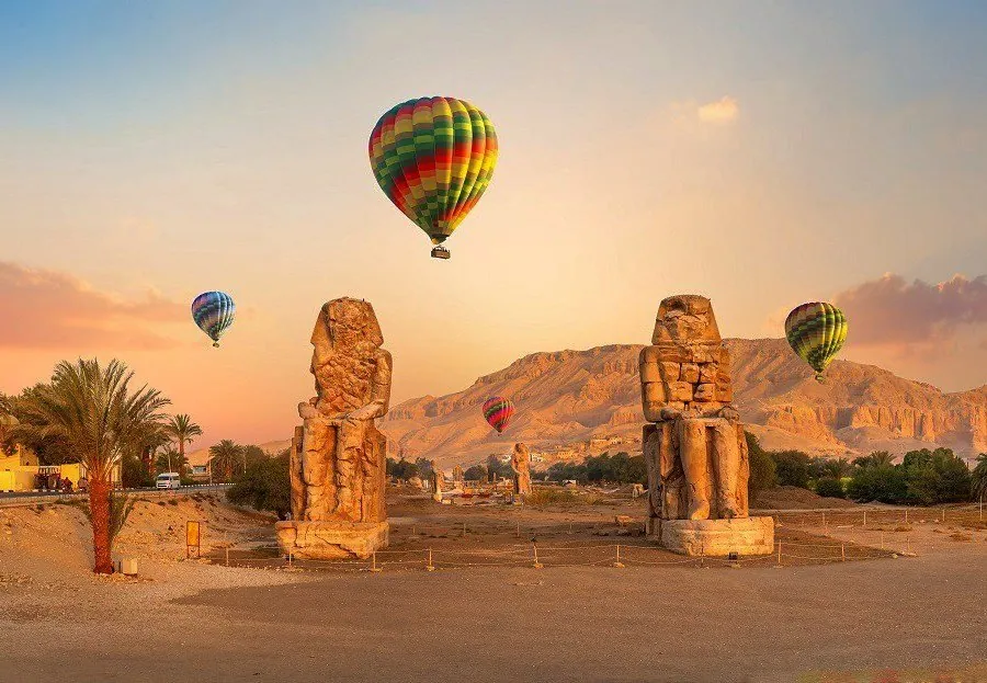 Hot air balloons rising over the Colossi of Memnon in Luxor at sunrise