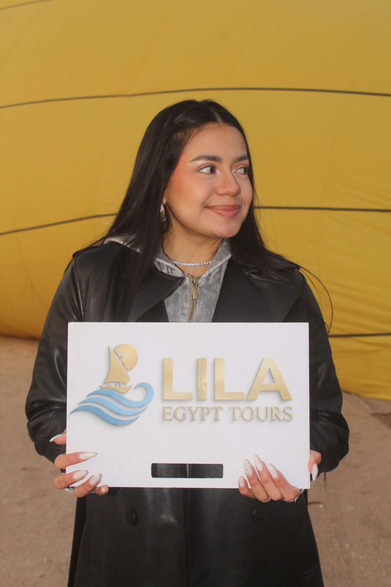A traveller holding the Lila Egypt Tours sign in front of a hot air balloon in Luxor